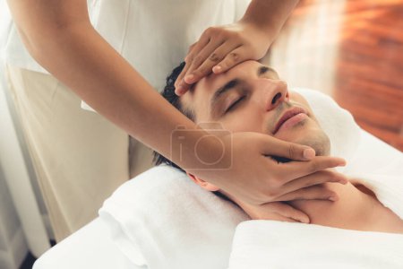 Foto de Hombre caucásico disfrutando de relajante masaje de la cabeza anti-estrés y mimar belleza facial recreación de la piel de ocio en dayspa ambiente de luz moderna en el complejo de lujo o salón de spa del hotel. Silencioso. - Imagen libre de derechos