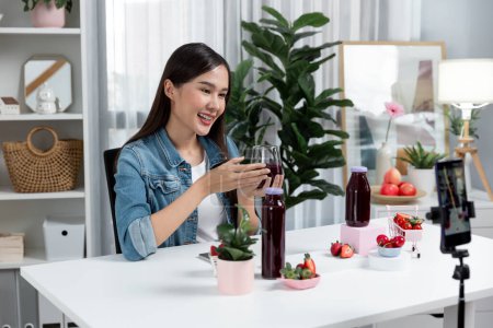 Photo for Smiling young beautiful Asian reviewing tasty mixed strawberry and cherry juice detox drinks, showing healthy product to promote for special promotion selling on social media online record. Stratagem. - Royalty Free Image