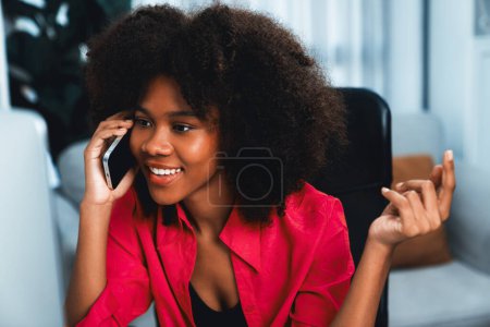 Foto de Mujer africana hablando con su compañero de trabajo o amigo por teléfono y mirando a la pantalla con la cara feliz. Logro para promover el puesto de trabajo en la empresa con la vida de las buenas noticias. Tastemaker. - Imagen libre de derechos