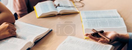 Photo for Close-up female Christian prayer pickup holy cross on bible book at wooden church table while asian believer reading bible. Concept of religion, faith, and god blessing. Warm background. Burgeoning. - Royalty Free Image