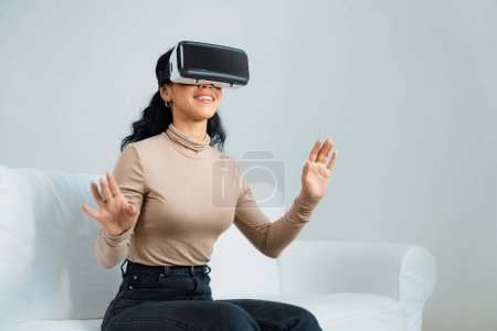 Téléchargez les photos : Jeune femme utilisant réalité virtuelle VR masque à la maison pour une expérience d'achat en ligne cruciale. L'innovation VR en réalité virtuelle optimisée pour le divertissement numérique féminin. - en image libre de droit