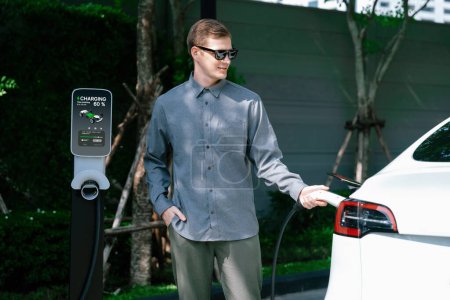 Photo for Young man travel with EV electric car charging in green sustainable city outdoor garden in summer shows urban sustainability lifestyle by green clean rechargeable energy of electric vehicle innards - Royalty Free Image