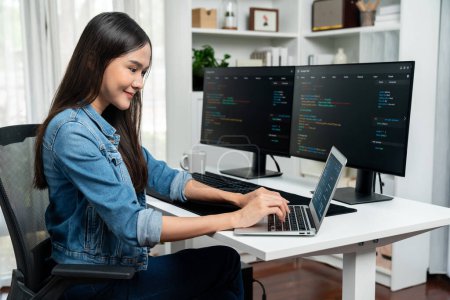 Photo for Smiling young Asian in IT developer creating with typing online information on laptop with coding program data of application, wearing jeans shirt. surrounded by safety analysis two screen. Stratagem. - Royalty Free Image