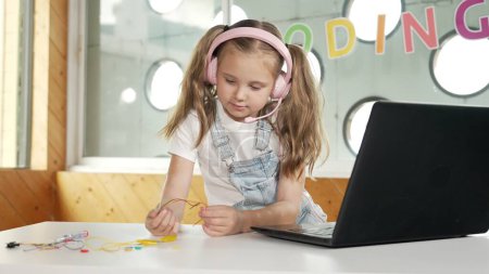 Photo for Pretty girl wearing headphone while study electronic equipment. Caucasian child doing science experiment while laptop, screwdriver and wires placed near on table. Smart online classroom. Erudition. - Royalty Free Image