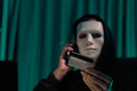 Photo for White criminal anonymous mask calling to credit card owner to threaten ransom with privacy information all database, making password encryption by programming hack trying to make insecure. Pecuniary. - Royalty Free Image