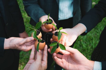 Grupo de empresarios que sostienen reputada cáscara de huevo transformada en maceta de fertilizantes, simbolizando el compromiso de nutrir y cultivar brotes o plantas de bebés como parte de un proyecto de reforestación corporativa. Gyre.