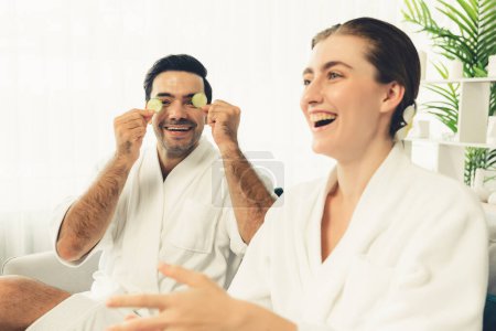 Photo for Blissful couple in bathrobe playing with cucumber and enjoying daylight ambiance spa salon resort or hotel during holiday. Pampering face spa and skincare treatment with essence relaxation. Quiescent - Royalty Free Image