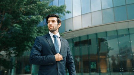 Photo for Handsome caucasian business man standing in front of building. Skilled investor looking around while pose cool at camera. Smart project manager wearing formal suit. Vision and professional. Exultant. - Royalty Free Image