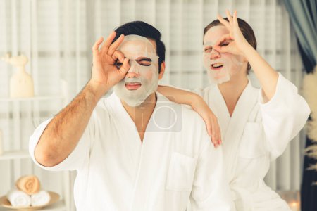 Téléchargez les photos : Ambiance moderne sereine de jour du salon de spa, couple client se livre à rajeunir avec masque de soins du visage. Traitement de la peau du visage et procédure de cosmétologie beauté pour le visage. Tranquillité - en image libre de droit