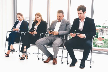Photo for Businesswomen and businessmen using mobile phone while waiting on chairs in office for job interview. Corporate business and human resources concept. uds - Royalty Free Image