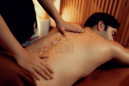Photo for Man customer having exfoliation treatment in luxury spa salon with warmth candle light ambient. Salt scrub beauty treatment in Health spa body scrub. Quiescent - Royalty Free Image