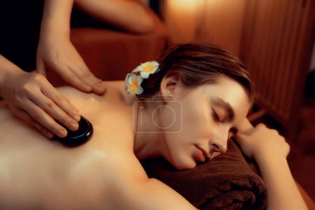 Photo for Hot stone massage at spa salon in luxury resort with warm candle light, blissful woman customer enjoying spa basalt stone massage glide over body with soothing warmth. Quiescent - Royalty Free Image