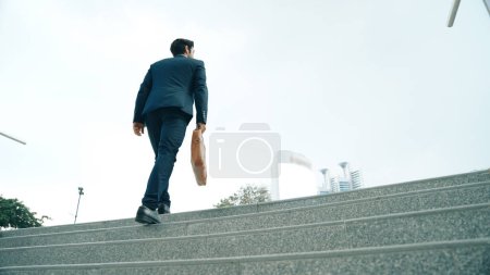 Foto de Vista superior del hombre de negocios inteligente subiendo escaleras con la bolsa en la mano. Gerente de proyecto profesional subir la escalera e ir al lugar de trabajo. Aumentar la habilidad, conseguir promoción, viajar. Exultante. - Imagen libre de derechos