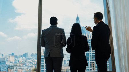 Photo for Back view diverse team of ambitious business people standing in ornamented office gazing out window to cityscape skyline. Determination and business ambition drive their career toward to bright future - Royalty Free Image