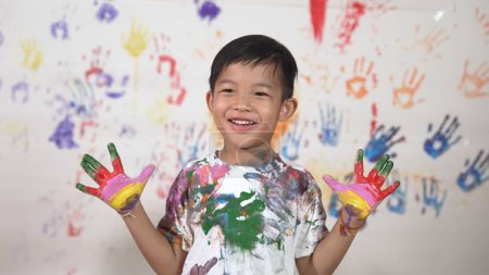 Photo for Asian happy student put hands up together show colorful stained hands. Smiling boy standing in front white background with stained hands while looking at camera. Creative activity concept. Erudition. - Royalty Free Image