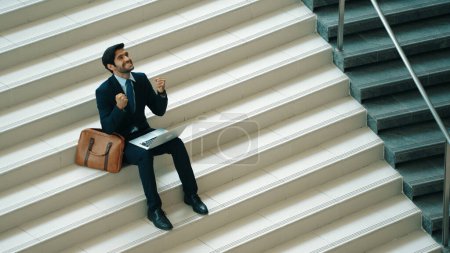 Photo for Top view business man celebrate successful project while sitting at stairs. Smart project manager getting new gob, getting promotion, increasing sales while calling friends by using laptop. Exultant. - Royalty Free Image