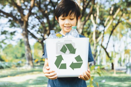 Photo for Cheerful young asian boy holding recycle symbol bin on daylight natural green park promoting waste recycle, reduce, and reuse encouragement for eco sustainable awareness for future generation. Gyre - Royalty Free Image