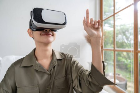 Foto de Mujer joven que usa gafas VR de realidad virtual en casa para una experiencia de compra en línea extrema. La innovación de realidad virtual VR optimizada para el estilo de vida de entretenimiento digital. - Imagen libre de derechos