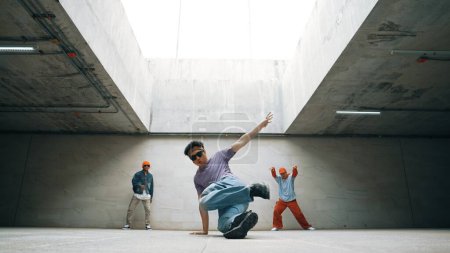 Téléchargez les photos : Groupe de hipster élégant effectuer la danse ensemble dans la construction. Happy break dancer aime passer à la musique hip hop avec la danse freestyle entouré par l'équipe de danseurs de rue. Sport de plein air 2024. Brillamment. - en image libre de droit