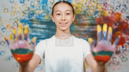 Photo for Portrait of happy smart student looking at camera while showing hand to camera with colorful color. Smiling caucasian teenager wearing white shirt while standing at colorful stained wall. Edification. - Royalty Free Image