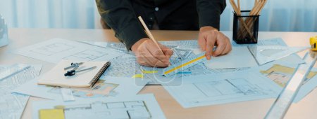 Photo for A portrait of architect using divider to measure blueprint. Architect designing house construction on a table at studio, with architectural equipment scattered around. Focus on hand. Delineation - Royalty Free Image