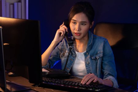 Photo for Young beautiful Asian creative woman calling on phone desk to customer or coworker explaining creator projects high profit while searching market analysis on pc at neon office at night. Stratagem. - Royalty Free Image