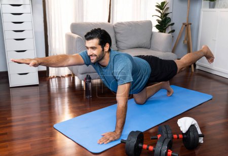 Photo for Flexible and dexterity man in sportswear doing yoga position in meditation posture on exercising mat at home. Healthy gaiety home yoga lifestyle with peaceful mind and serenity. - Royalty Free Image