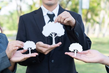 Téléchargez les photos : Un groupe d'hommes d'affaires tenant un arbre en papier blanc met en valeur la protection de l'environnement en cultivant la nature, en réduisant les émissions de CO2 et de gaz à effet de serre grâce au reboisement pour un avenir plus vert. Pneumatique - en image libre de droit