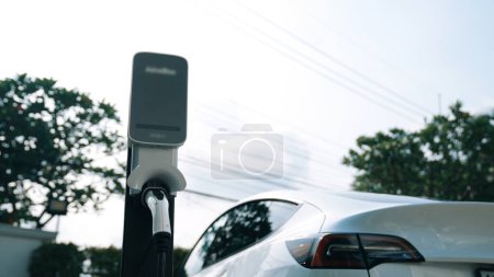Téléchargez les photos : Batterie de recharge de voiture électrique EV au parking dans le parc naturel vert de la ville. Technologie d'énergie propre alternative pour une automobile rechargeable pour des déplacements urbains durables et respectueux de l'environnement. Synchronos - en image libre de droit