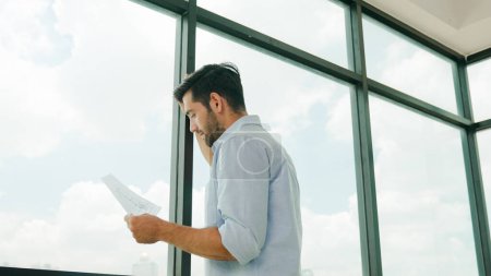 Photo for Architect engineer looking at blueprint near window with cityscape. Professional interior designer looking blueprint while planing, thinking, designing, preparing about building project. Tracery - Royalty Free Image