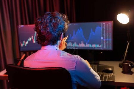 Photo for Young investor in stock trader pointing on dynamic exchange rate on screens in market graph online in real time at neon light modern office at night time, analyzing financial technology data. Gusher. - Royalty Free Image