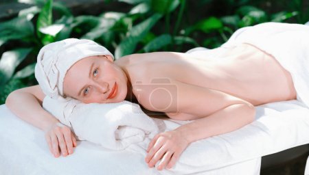 Foto de Una hermosa mujer joven se encuentra en una cama de spa mientras mira a la cámara. Sensación de relajación y paz. Atractiva mujer caucásica rodeada de los tranquilizantes sonidos de la naturaleza. Tranquilidad - Imagen libre de derechos