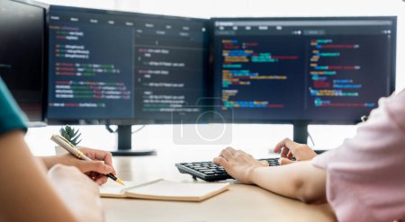 Photo for Female programer taking a note while young skilled web developer present program while computer displayed program code at modern office company. Java script, web design concept. Burgeoning. - Royalty Free Image