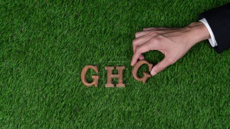 Foto de Coloque a mano el texto del alfabeto de madera en GHG sobre el fondo de hierba verde biofílica como símbolo ecológico para alentar el mensaje para la campaña de reducción de emisiones de gases de efecto invernadero y la conciencia ambiental. Gyre. - Imagen libre de derechos