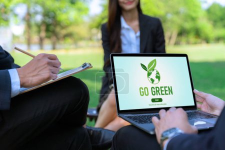Foto de Grupo de empresarios asiáticos que planean un plan de desarrollo respetuoso con el medio ambiente en la pantalla del portátil y un proyecto de tecnología sostenible para un futuro más verde, eco oficina al aire libre en el parque natural. Gyre. - Imagen libre de derechos