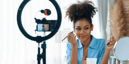 Téléchargez les photos : Femme influenceur tirer en direct vlog revue vidéo maquillage médias sociaux cruciaux ou blog. Heureuse jeune fille avec éclairage de studio cosmétique pour la diffusion de session d'enregistrement marketing en ligne. - en image libre de droit
