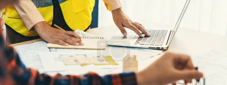 Photo for Cropped image of professional engineer team working on blueprint while his coworker working on laptop at meeting table with blueprint and wooden block scattered around. Closeup. Delineation. - Royalty Free Image