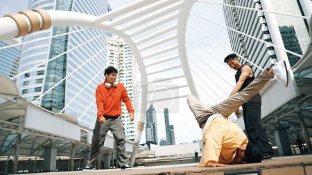 Foto de Grupo de profesionales feliz bailarina callejera animar mientras asiático hipster realizar b boy dance en la ciudad urbana rodeado de personas con bajo ángulo de la cámara. Rompe el concepto de baile. Deporte al aire libre 2024. Rígidamente.. - Imagen libre de derechos