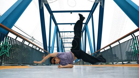 Photo for Hipster perform b-boy footstep and street dance at bridge with background. Professional break dancer wear stylish cloth and looking at camera while pose at camera. Outdoor sport 2024. Sprightly. - Royalty Free Image