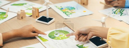 Photo for A cropped picture of green city poster was placed at green business meeting on meeting table with environmental document, wooden house block and windmill model scattered around. Closeup. Delineation. - Royalty Free Image