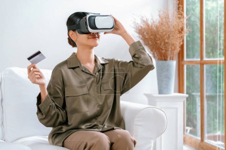 Foto de Mujer joven que usa gafas VR de realidad virtual en casa para una experiencia de compra en línea extrema. La innovación de realidad virtual VR optimizada para el estilo de vida de entretenimiento digital. - Imagen libre de derechos