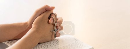 Photo for Asian male folded hand prayed on holy bible book while holding up a pendant crucifix. Spiritual, religion, faith, worship, christian and blessing of god concept. Blurring background. Burgeoning. - Royalty Free Image