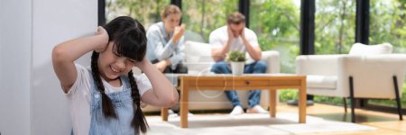Stressed and unhappy girl huddle in corner, cover her ears with painful expression while her parent arguing in background. Domestic violence and traumatic childhood depression. Panorama Synchronos