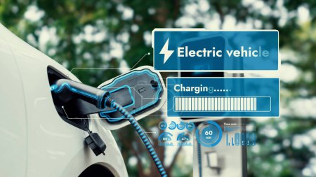 Photo for Electric car plug into EV charger cable from charging station display smart digital battery status hologram in eco green park and foliage background. Energy sustainability technological advance.Peruse - Royalty Free Image