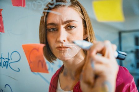 Photo for Closeup of young beautiful caucasian business leader presents marketing idea while writing marketing idea on glass board with mind map and colorful sticky notes. Portrait. Brainstorm. Immaculate. - Royalty Free Image