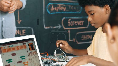 Photo for Cute african boy learning to use electronic tool while laptop display code while teacher talking about writing engineering prompt. Diverse children coding program to fixing car model. Edification. - Royalty Free Image