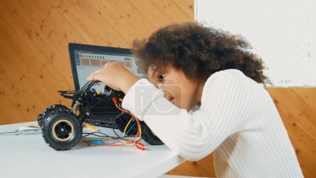 Photo for Smart african girl build robotic car while using wires while using laptop setting or writing prompt code. Skilled female student working on computer in STEM technology online classroom. Erudition. - Royalty Free Image