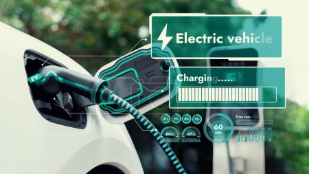 Téléchargez les photos : Fiche de voiture électrique dans le câble de chargeur EV de la station de charge affichent l'hologramme numérique intelligent d'état de batterie dans le parc vert écologique et le fond de feuillage. Progrès technologiques en matière de durabilité énergétique. - en image libre de droit
