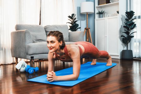 Photo for Athletic and sporty woman doing plank on fitness mat during home body workout exercise session for fit physique and healthy sport lifestyle at home. Gaiety home exercise workout training. - Royalty Free Image