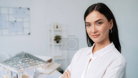 Photo for Close up portrait of young beautiful professional architect engineer cross arms and poses confidently with house model at white modern office with blueprint. Creative living and design. Immaculate. - Royalty Free Image